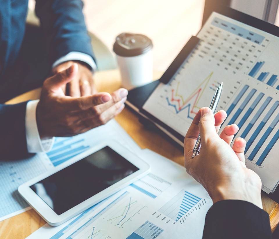 Two professionals discussing financial charts and graphs on a tablet and laptop, highlighting outsourced accounting services